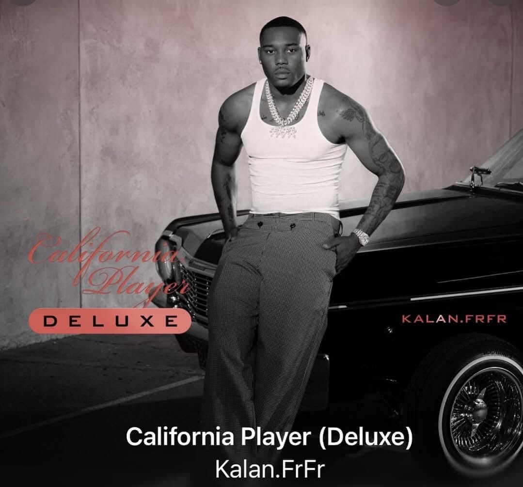 Album cover for Kalan.FrFr's 'California Player (Deluxe)'. K leans against a classic black lowrider car, wearing a white tank top, a chain, and dress pants. The background is a wall with the album title written in red script and block letters. 